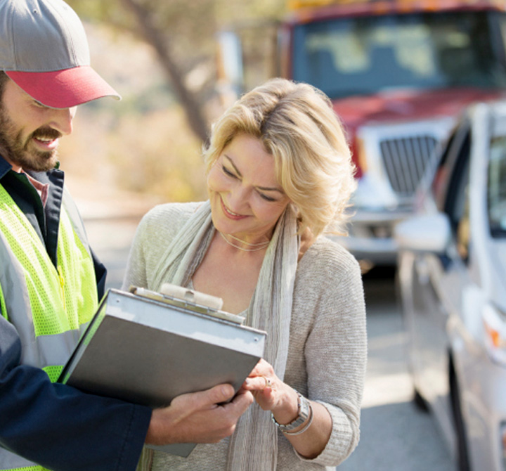 Woman signing paperwork outside by her car with a towtruck driver. 
