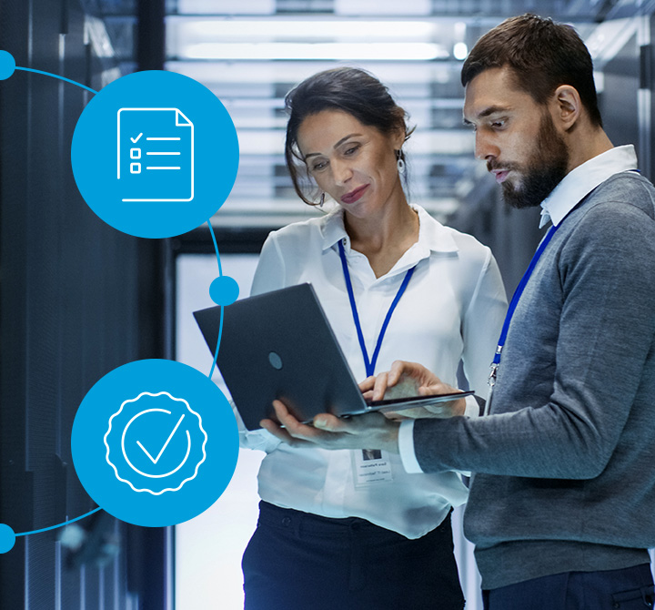 A man and woman in a server room working on a laptop.