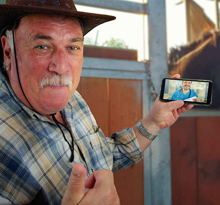 Male wearing a cowboy hat on a farm, video chatting with a healthcare professional