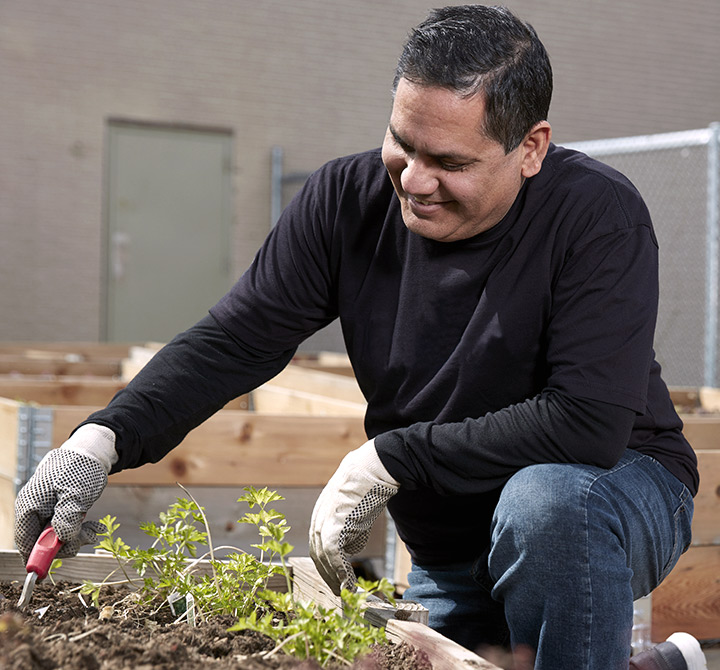 Landscape person in a black shirt wearing white gloves digging in a wooden garden box.