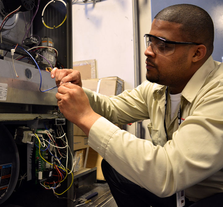 A Lincoln Tech student, wearing safety glasses, is working on the wiring on an HVAC system as part of the education track.