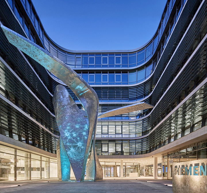 A courtyard view of the Siemens Headquarters office park in Munich featuring a large abstract statue in the center. 